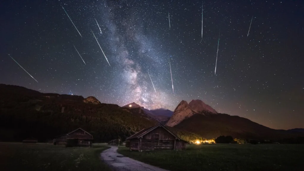 Perseidi nel cielo notturno estivo con scie luminose sopra un paesaggio buio